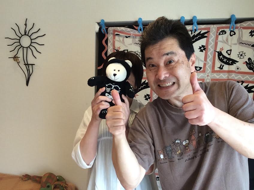 顔を熊のぬいぐるみで隠した女性のお客様と前田歩の笑顔のツーショット写真